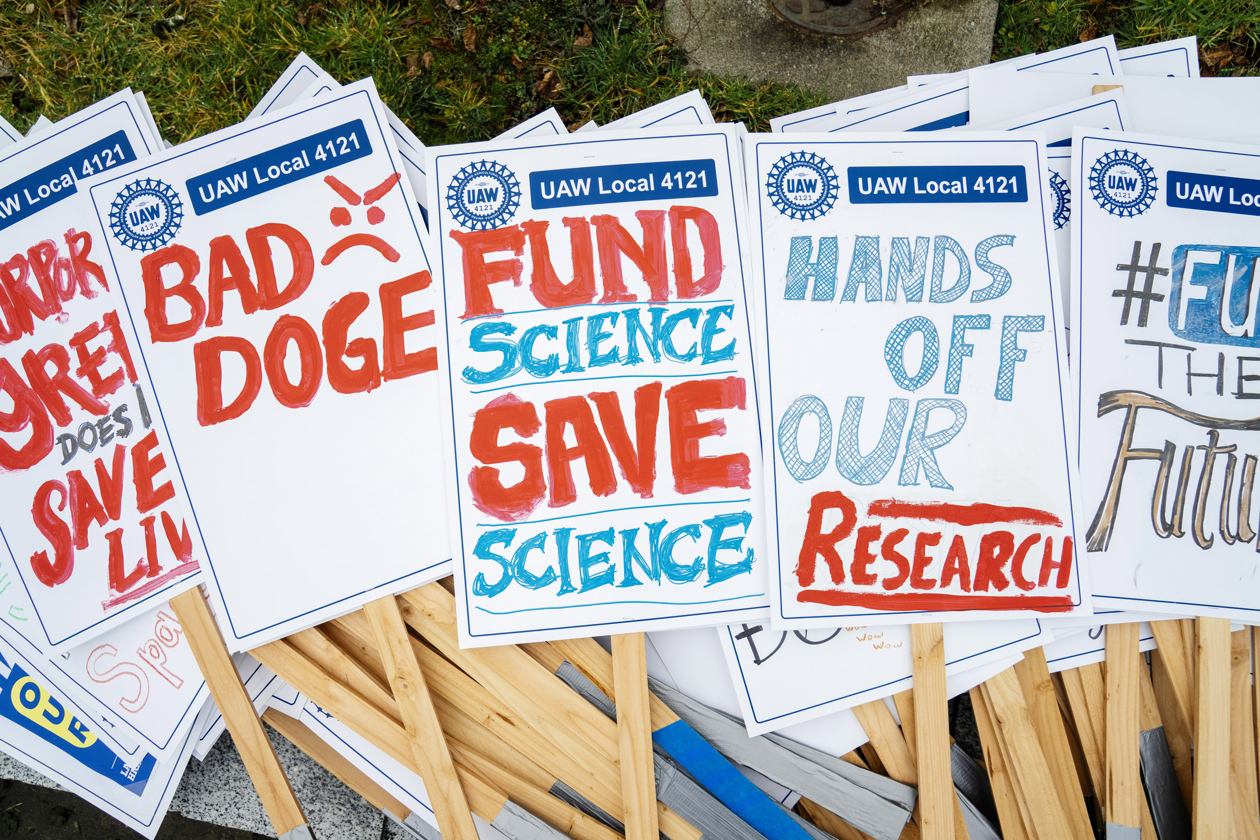 Protest signs lay in a pile before a large crowd of academic workers, staff, faculty, and community supporters gathers for a rally organized by the UAW Local 4121 to oppose Trump administration funding cuts to the National Institute of Health in Seattle, Washington, USA, on Wed., Feb. 19, 2025. The Trump administration, through Elon Musk's Department of Government Efficiency (DOGE) has proposed cuts to the NIH which opponents argue would put a stop to medical research around the country. Speakers at the event spoke about colleagues who had lost jobs already because of cuts and threats to the progress of their research.