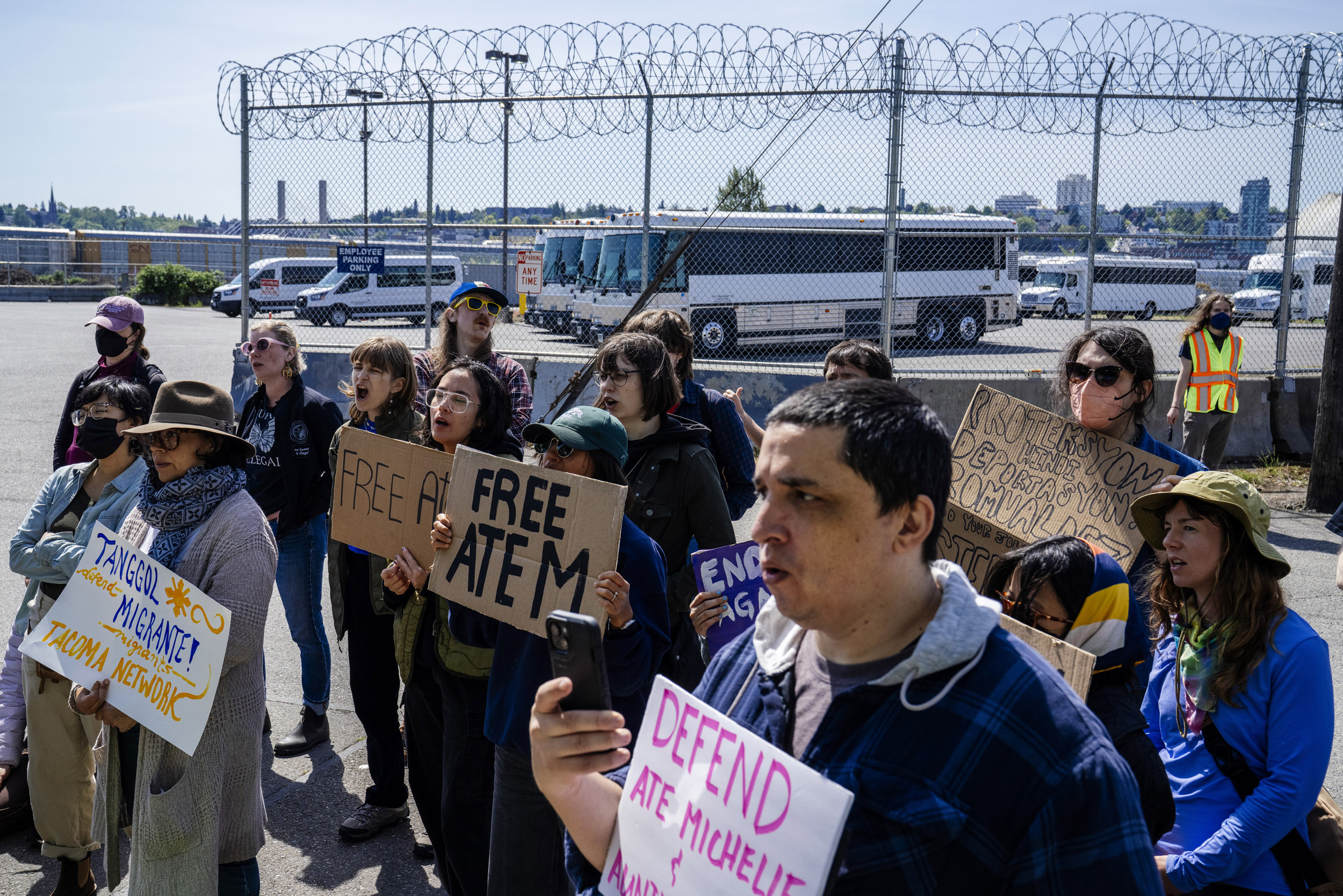 Tanggol Migrante activists and supporters gather outside the Northwest Detention Center to rally in support of detained Filipina immigrants Ate Michelle, Lewelyn Dixon, and other detainees in Tacoma, Washington, USA, on Wed., April 30, 2025. Ate Michelle is a green card holder and mother of three; Lewelyn Dixon has had her green card for more than 50 years. Both women are being held by Immigration and Customs Enforcement at the Tacoma facility. Tanggol Migrante is calling for their release and for the Filipino government to support citizens in detention.  A razor-wire surrounded parking lot behind the rally is used to store Geo Group buses and vans used to transport detainees.