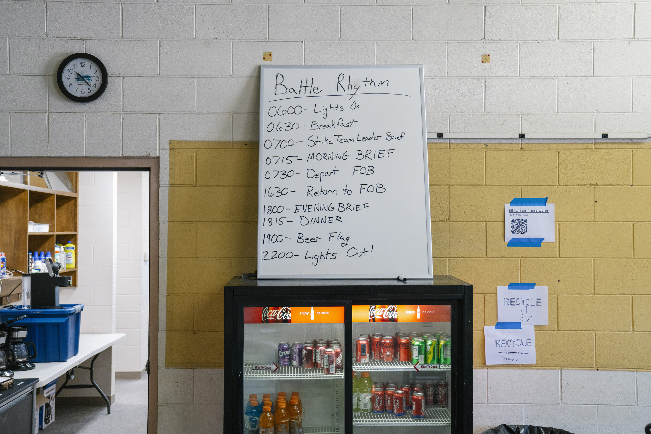 A whiteboard displays the "Battle Rhythm" schedule of Team Rubicon's daily activities and work in the old Kennewick Fire Station, called the "Forward Operating Base" by Team Rubicon, during a fire mitigation project in Zintel Canyon in Kennewick, Washington, USA, on Wed., May 1, 2024. The "Forward Operating Base" is where the teams organize their work, hang out, and sleep, throughout the operation. A crew of about 30 people has been working to remove burnable materials, including standing trees and brush, organized by the Team Rubicon disaster response volunteer organization.