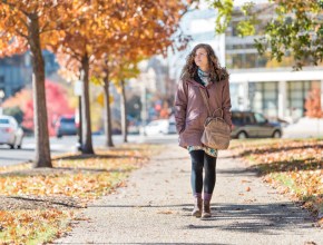 Young happy woman on sidewalk street walking in Washington DC, USA United States in alley of golden orange yellow foliage autumn fall trees on road during sunny day