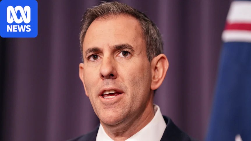 A man in a suit speaks at a press conference with an Australian flag in the background