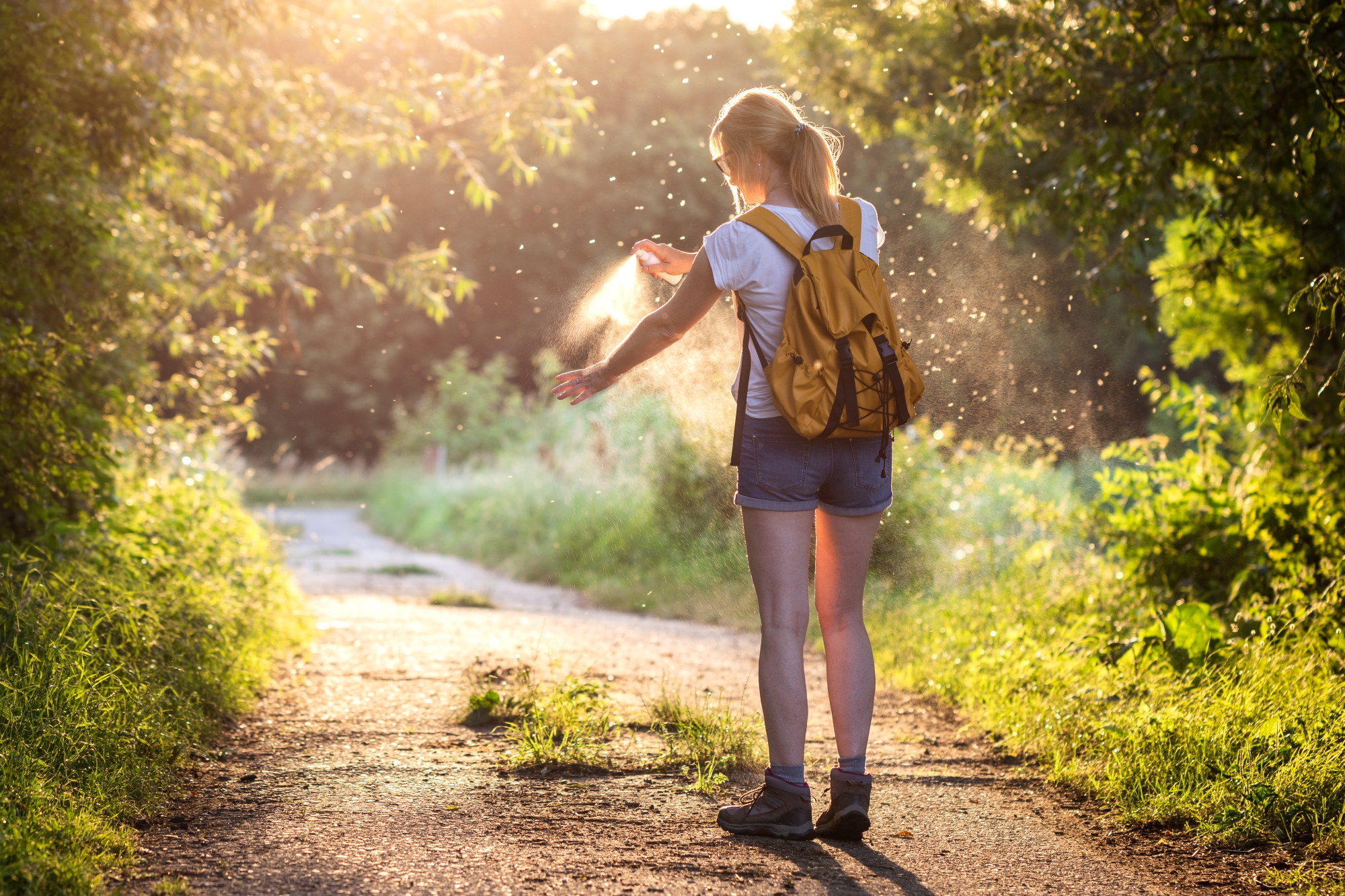 A woman sprays herself with bug spray.