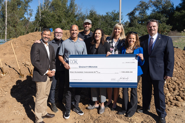 A group of people hold a large check for $100,000 for DignityMoves.