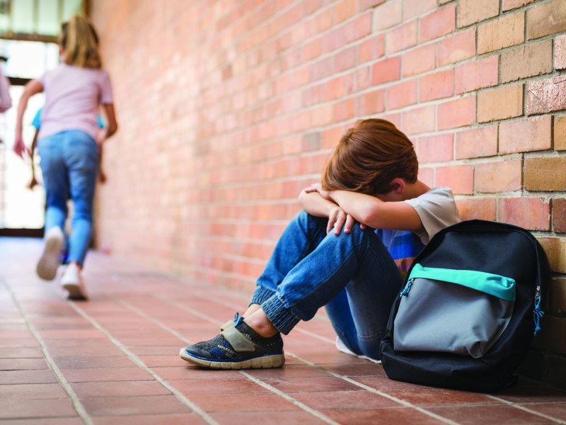 Sad young schoolboy sitting on corridor with hands on knees and head between his legs. (Green Shoot Media photo)