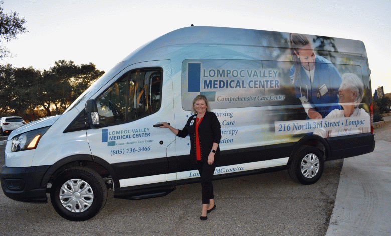 Comprehensive Care Center administrator Lorraine Jones shows off the new white patient van that has a picture of a medical caregiver wearing blue scrubs who is assisting a patient. (Courtesy photo)