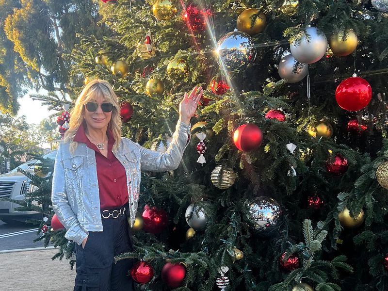 Coast Village Association executive director Beth Sullivan with the 35-foot Nordmann fir Christmas tree that stands at the heart of the street’s holiday celebration.