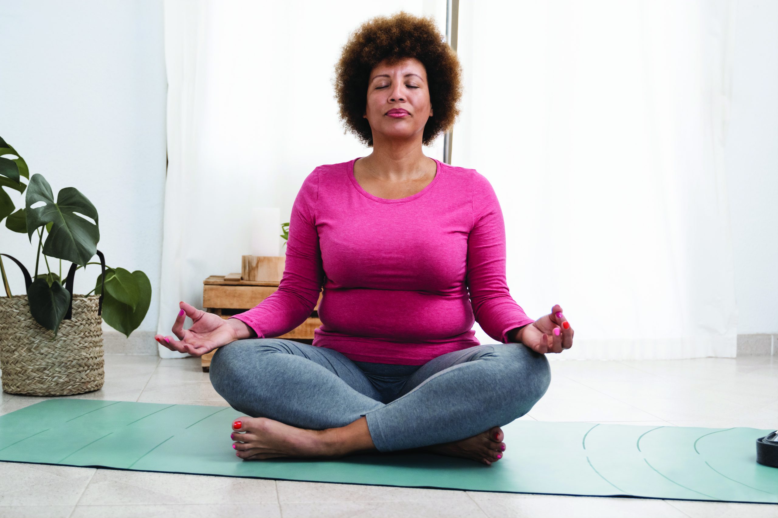 African senior woman doing pranayama breath exercises during yoga session at home.