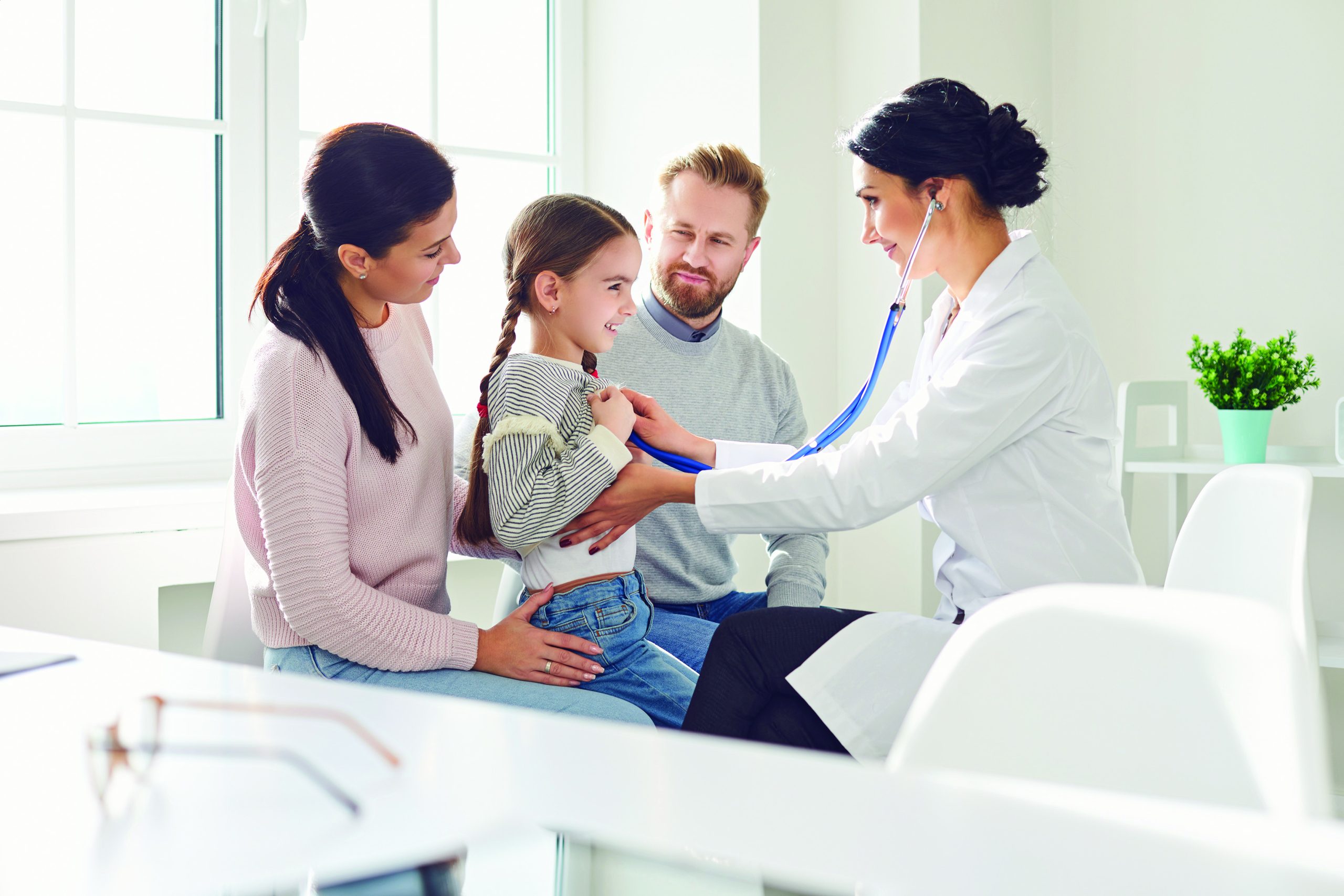 Happy family on a visit to the doctor in the office of a doctor. Woman family doctor sitting at the table with smiling family at the clinic.