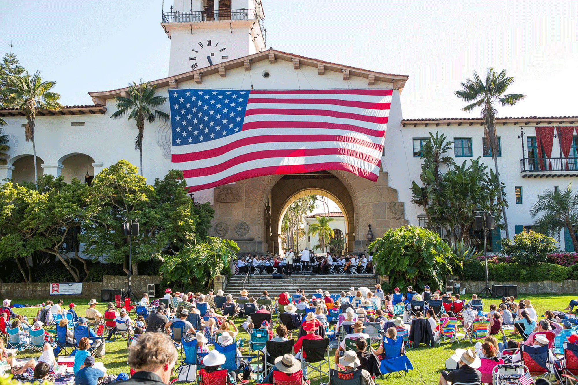 A huge American flag flies over the County Courthouse as the Fourth of July crowd sits on camping chairs listening to patriotic music. (Courtesy photo)
