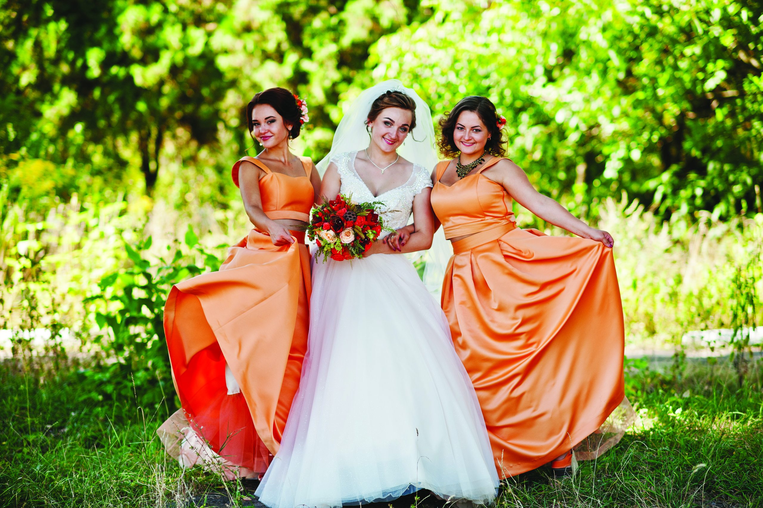 Happy bride having fun with her cool fun bridesmaids in the park on a wedding day.