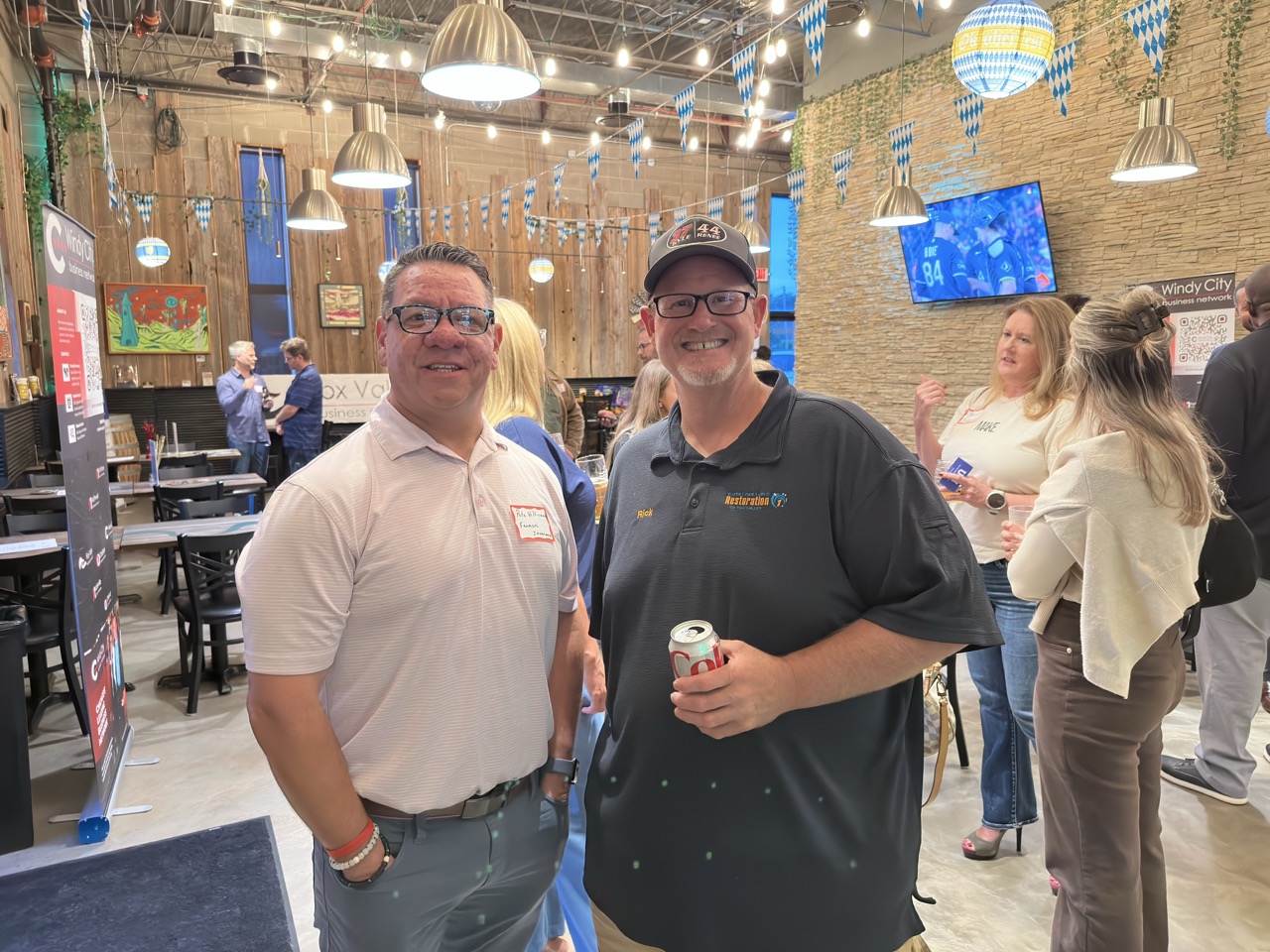 Two attendees pose with drinks, a Fox Valley Business Network banner on the wall behind them