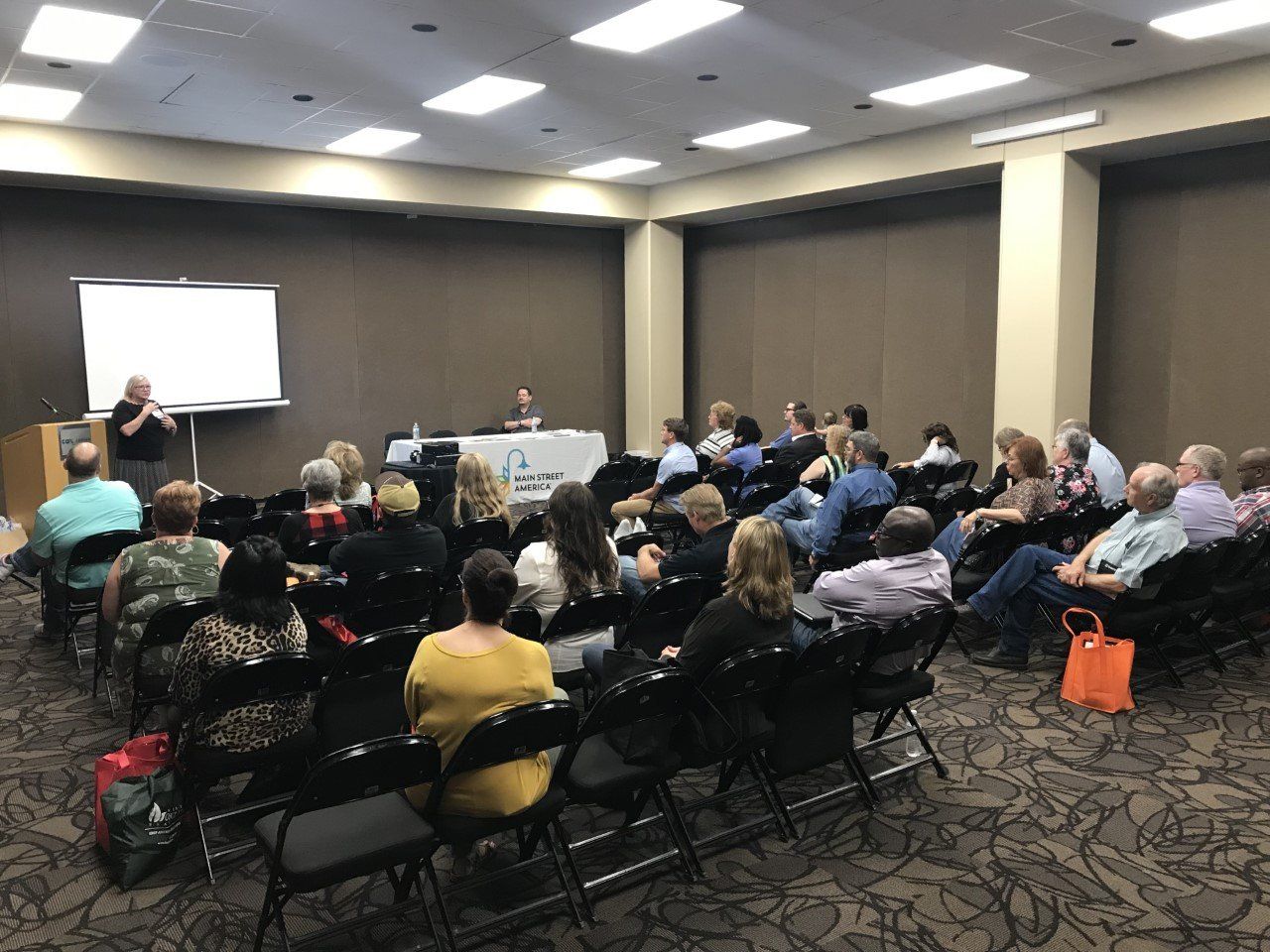 Buffy Skee, Director of Oklahoma Main Street, standing at the front of a conference room full of people sitting in chairs at the Main Street Application workshop.