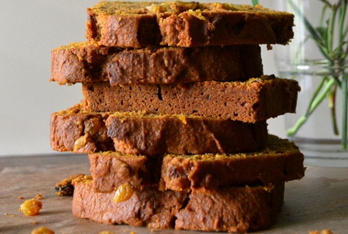 Sliced Pumpkin and Maple Spice Quickbread on a wooden board, revealing pecans and golden raisins, ready to be served.