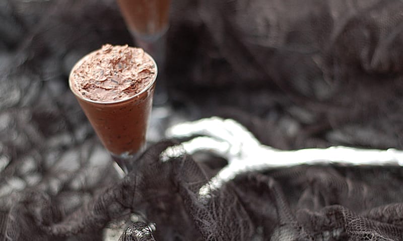A dark, almost black, bowl of Gruesome Vegan Forbidden Rice Halloween Pudding, topped with melted chocolate chips, ready for a spooky celebration.