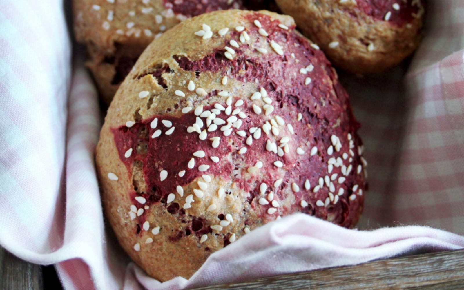 A sliced loaf of Marbled Beet Spelt and Buckwheat Bread, revealing vibrant pink and light brown swirls, sprinkled with sesame seeds.