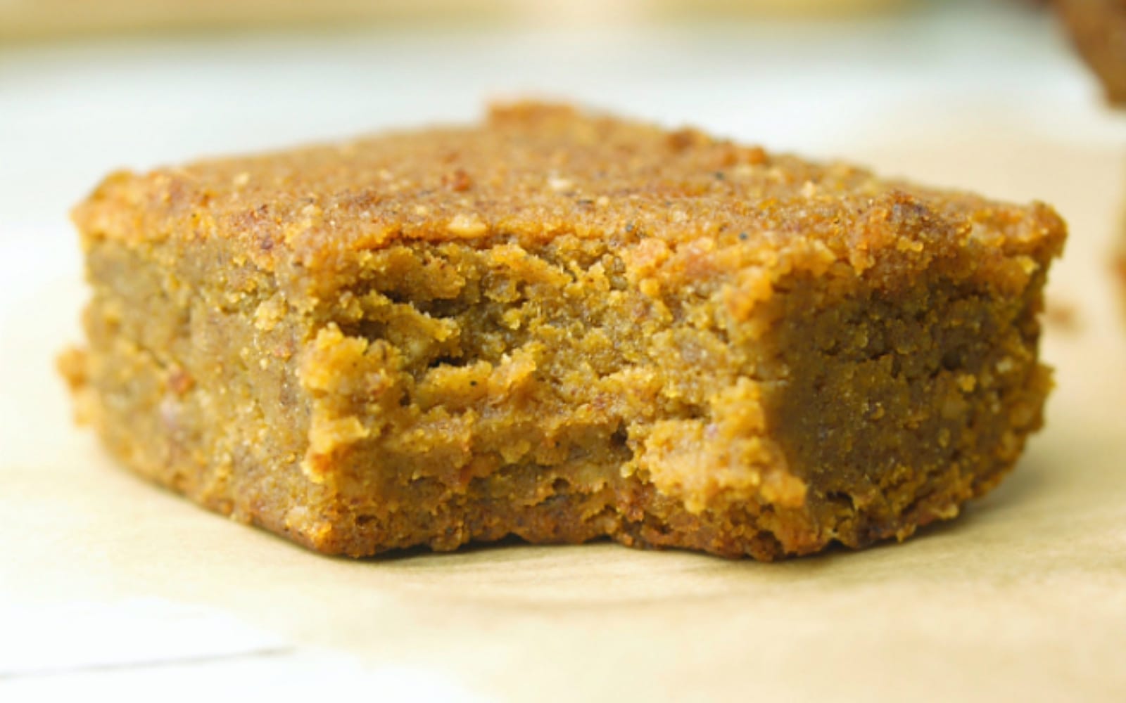 A square of moist pumpkin spice blondie, topped with a dusting of cinnamon, on a rustic plate, showcasing its soft, dense texture.