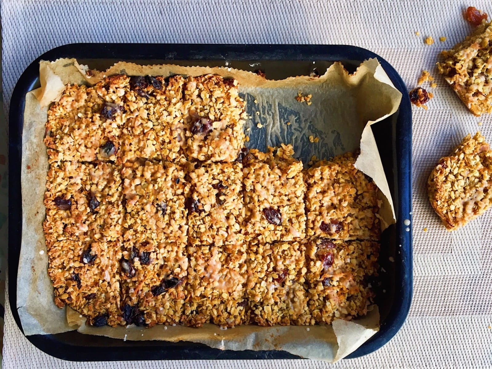 Close-up of golden brown vegan carrot and raisin flapjacks, cut into squares and drizzled with white cinnamon icing, on a baking tray.