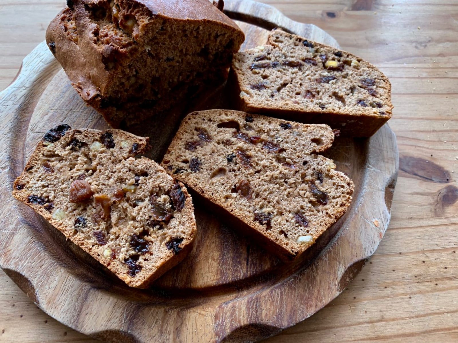 Slices of warm vegan Maple Chai Tea Loaf, studded with dried fruit, served on a plate with a cup of tea and a small dish of vegan butter.