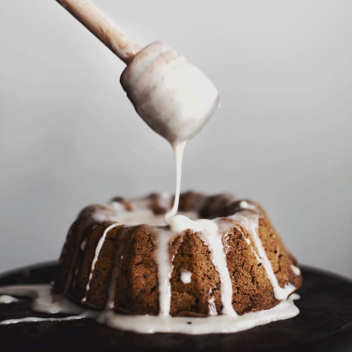 A trio of golden-brown Mini Ginger-Spiced Bundt Cakes, lightly dusted with powdered sugar, arranged on a rustic wooden board.