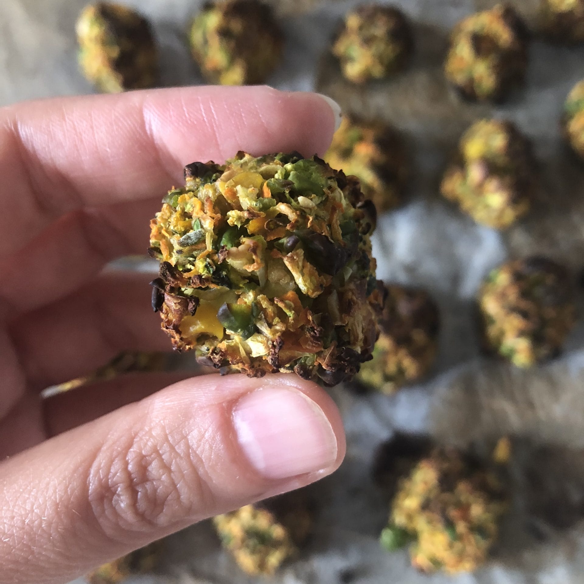 Several golden-brown, crispy baked vegan veggie balls, made with carrots, zucchini, peas, and corn, piled on a plate, garnished with fresh herbs.