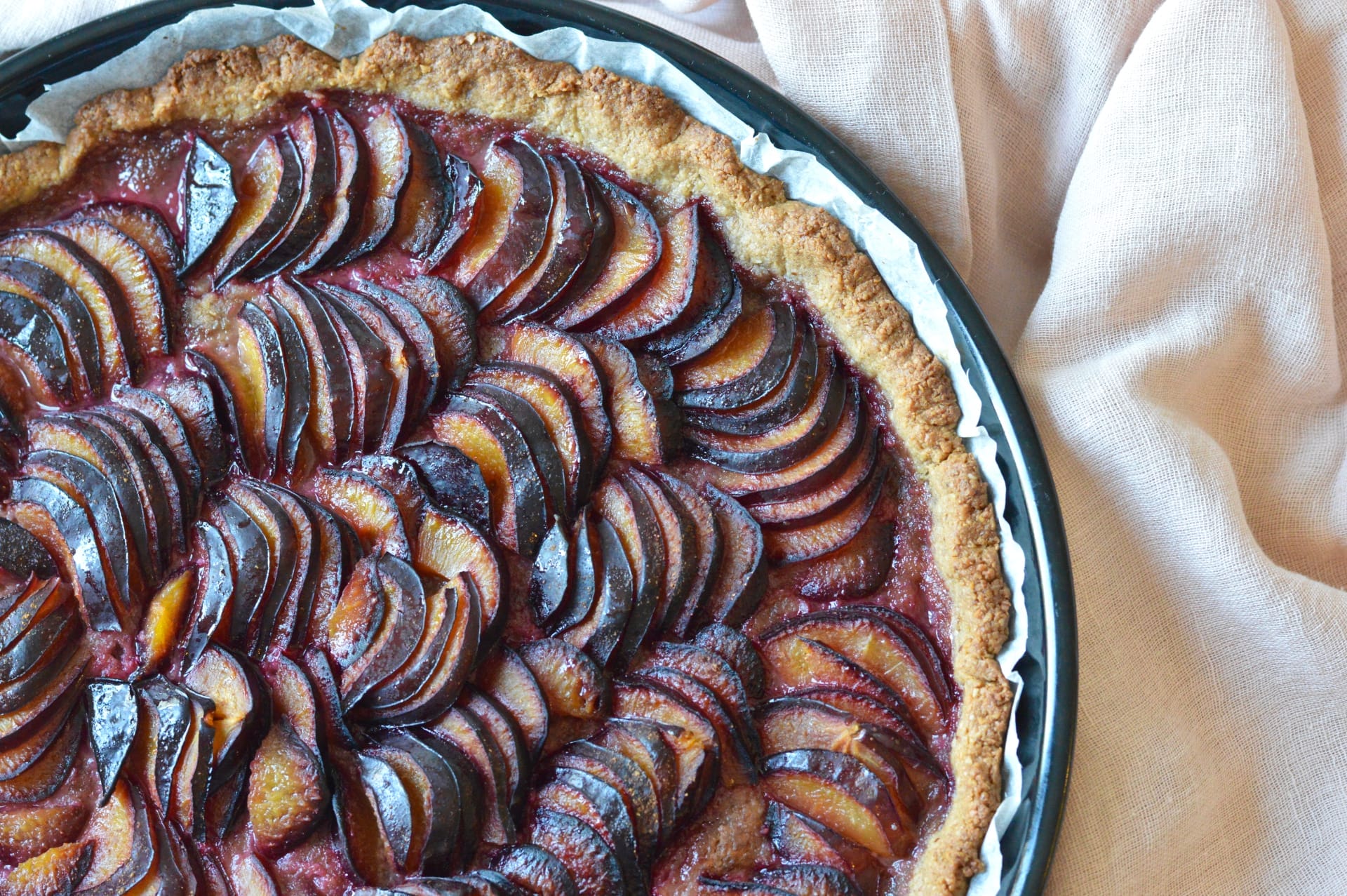 A golden-brown vegan and gluten-free plum pie, with a crispy oat-pecan crust and thinly sliced, juicy Italian plums, cooling on a rack.