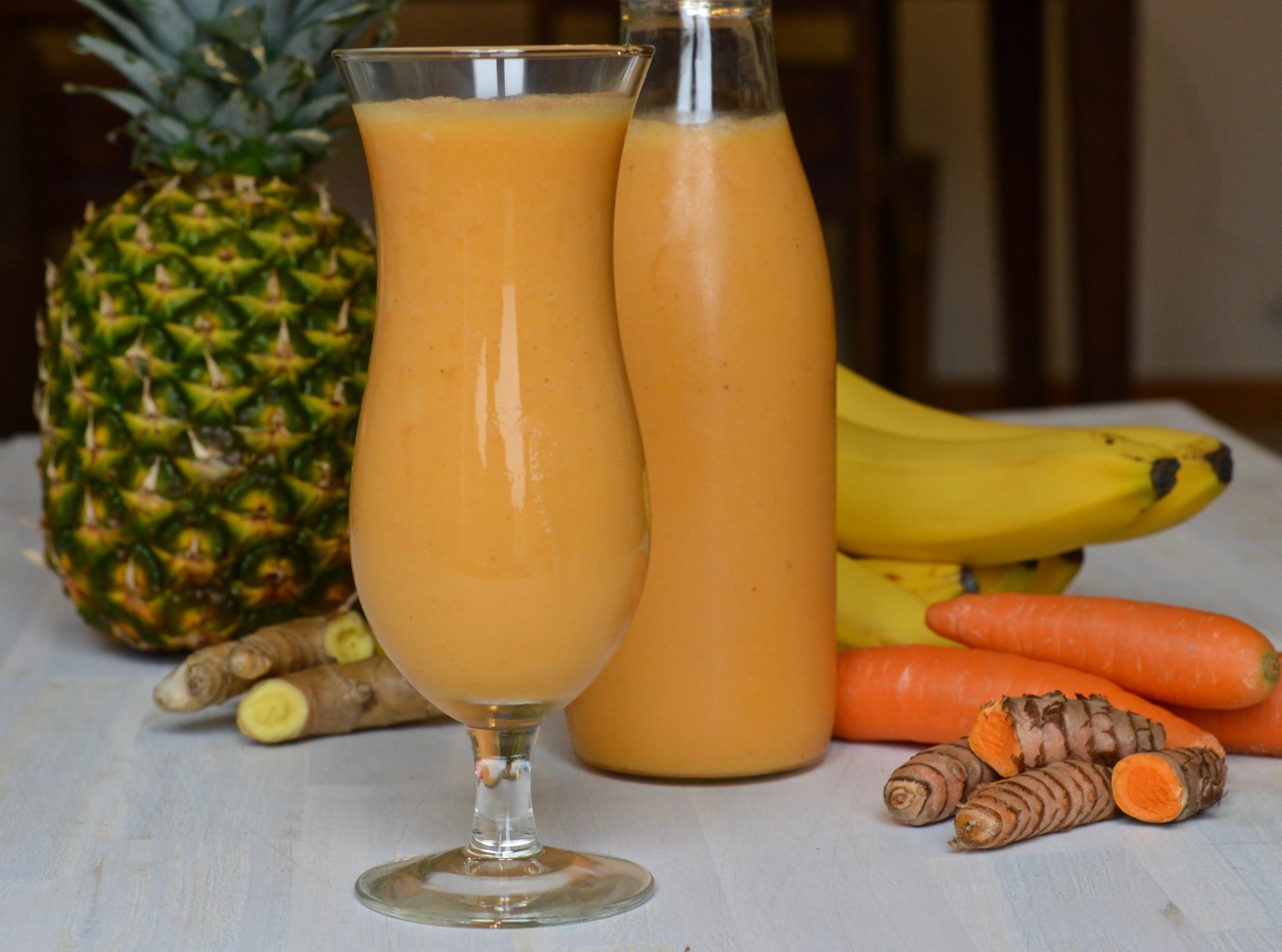 A vibrant orange-yellow Health Promoting Smoothie, made with carrots, pineapple, ginger, and curcuma, served in two clear glasses with ice.