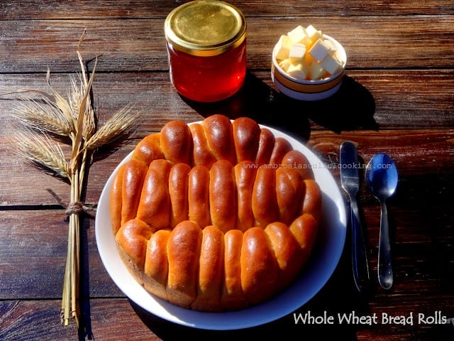 A round pan filled with warm, golden-brown vegan whole wheat bread rolls, freshly baked and brushed with melted plant-based butter, ready for serving.
