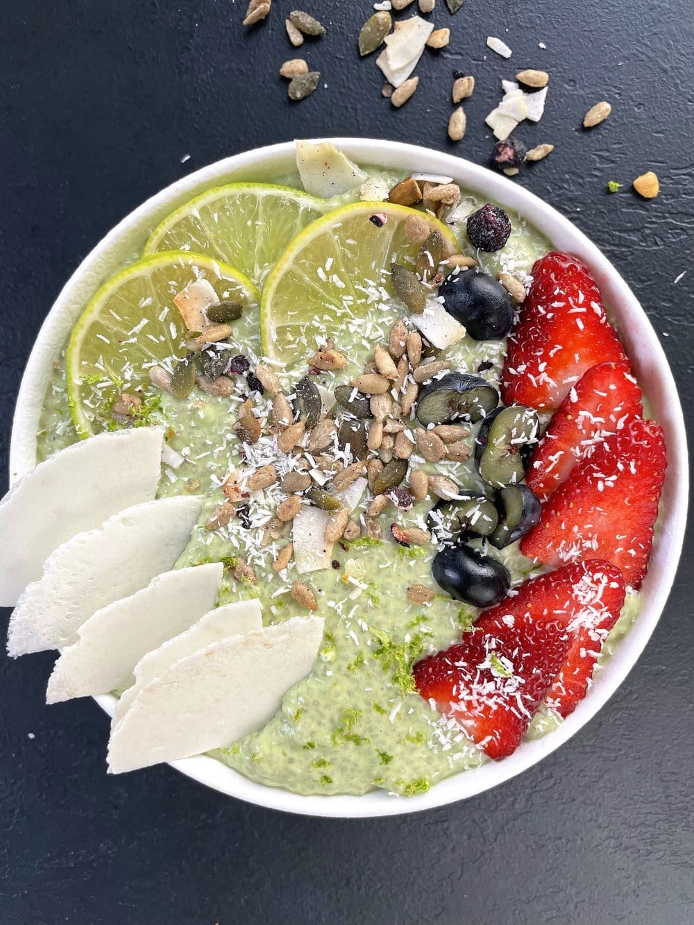 A vibrant green vegan Key Lime Pudding served in a clear jar, topped with fresh berries, lime slices, and zest.
