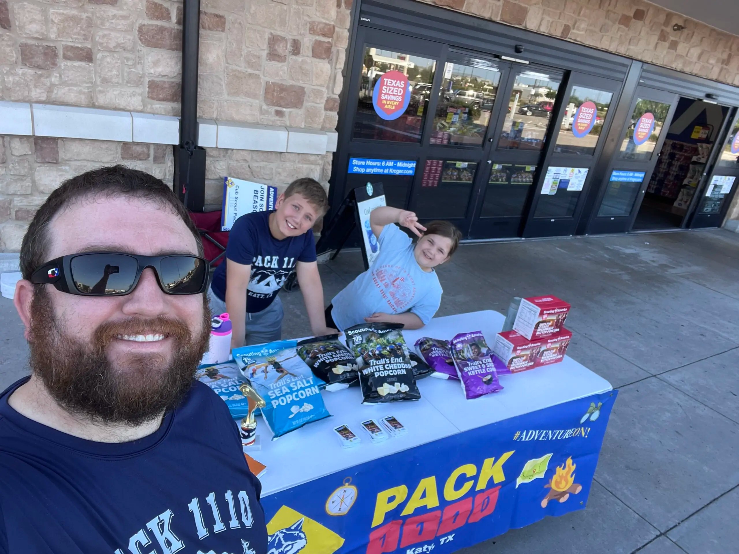 Scouts in front of a store selling popcorn with their dad.