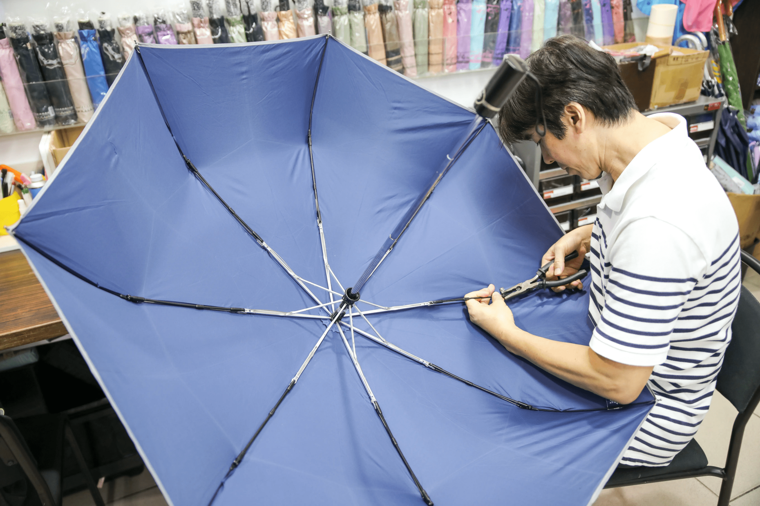雨之情保固維修服務 雨之情師傅坐在椅子上,低頭修理壞掉的藍色雨傘