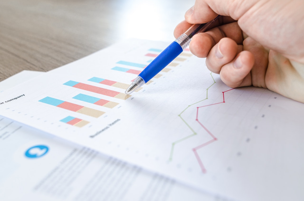 A pen hovers over business charts. / Photo via Lukas via Pexels / Used under license