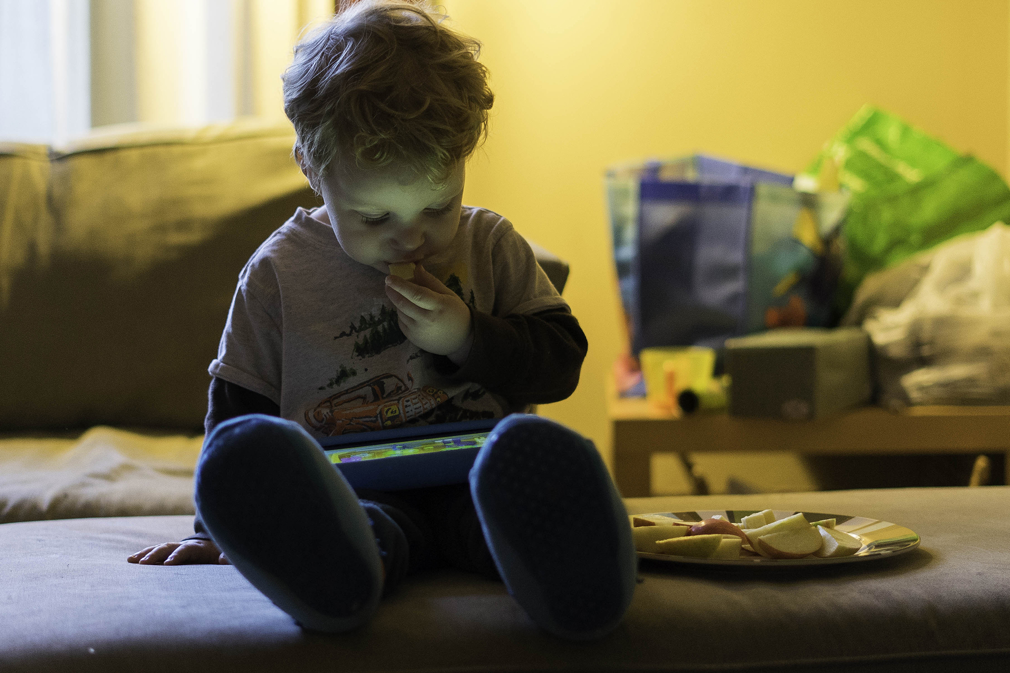 Oren Lev, 2, snacks on an apple during his allotted “screen time” at the family’s Point Breeze home. When he was 1, a pediatrician detected lead in his blood. (Photo by Aaron Warnick/PublicSource)