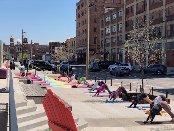 People practice yoga positions on a sidewalk area outside on a sunny day.