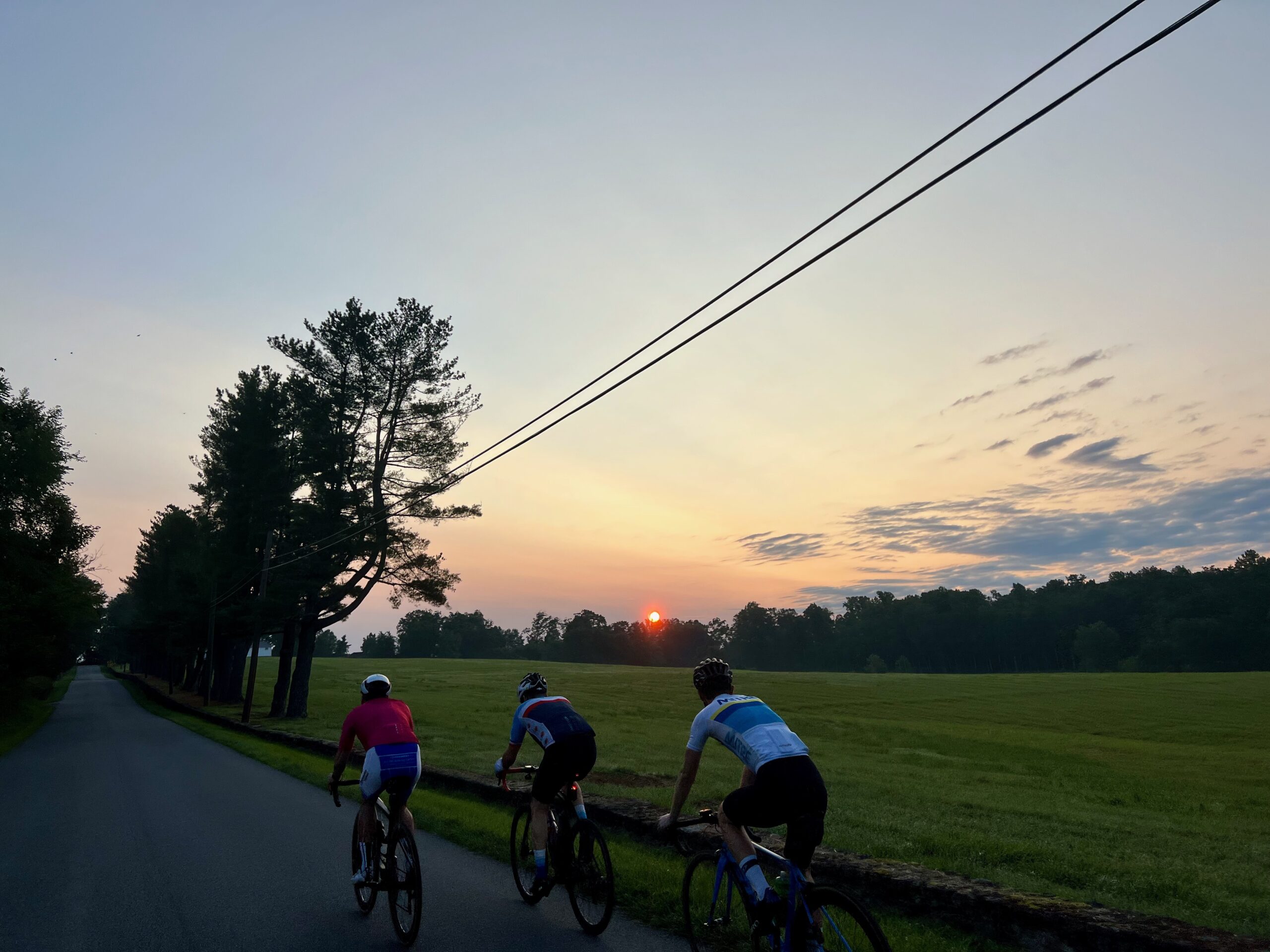 Three people riding bicycles on Ortman Road at sunrise