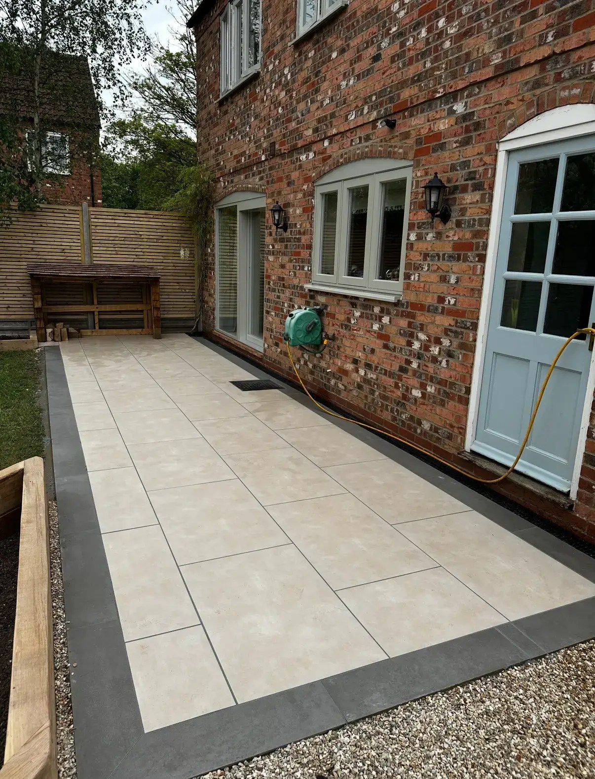Cream porcelain patio with dark border installed in Landscape gardeners in Lincoln, alongside red brick house and lawn