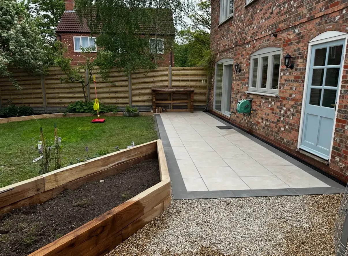 Porcelain patio installation with dark border and raised sleeper beds in Lincoln by Landscape gardeners.