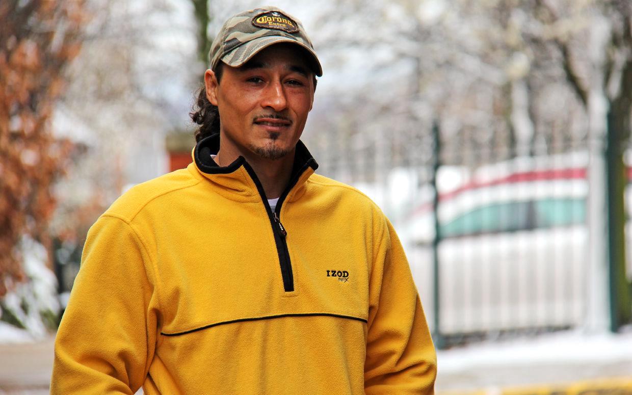 A man stands in a yellow jacket and camouflage baseball cap.