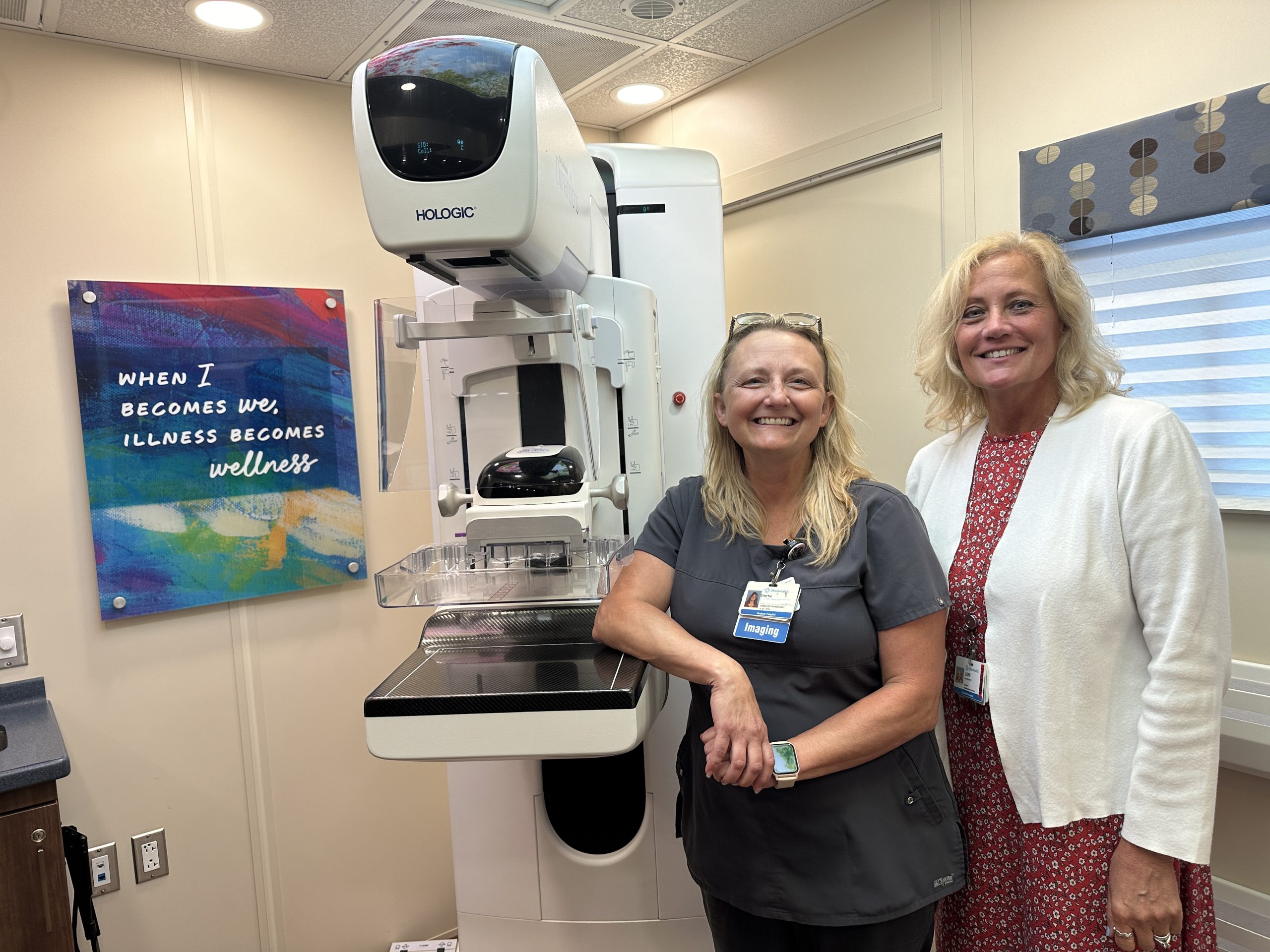 Two women pose for a photo next to a mammogram screening unit