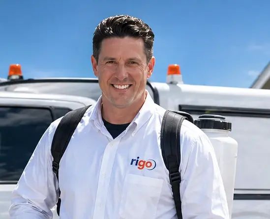 Smiling man in white polo shirt with rigo logo standing in front of service vehicles