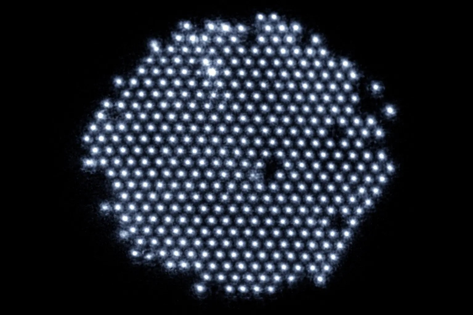 Representación artística de átomos como esferas brillantes en azul y naranja sobre fondo oscuro.