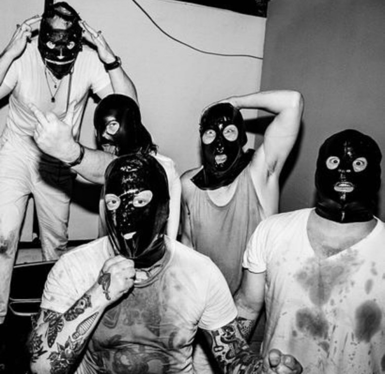 Tear Dungeon poses in gimp masks and b lood-stained white shirts for this black and white photo.