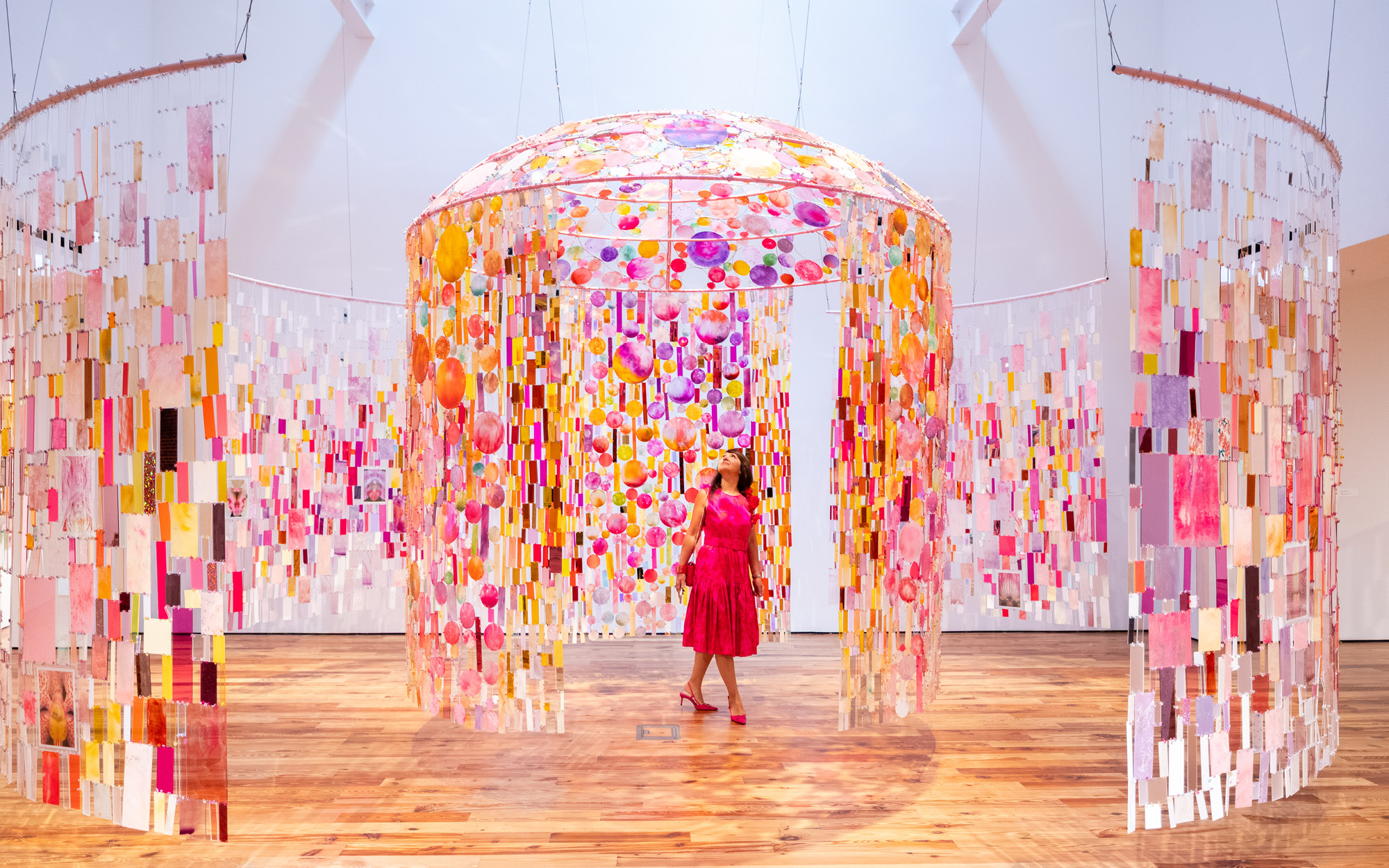 Visitors walking through a large glass installation artwork hanging in a large white gallery space.