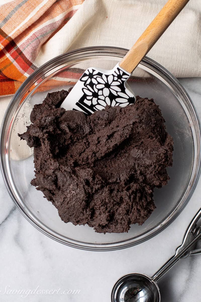 A bowl of black cocoa cookie dough with a spatula.