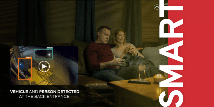 Couple relaxing on a sofa in a living room; inset security footage reads 'Vehicle and person detected at the back entrance' with a red SMART banner along the side.