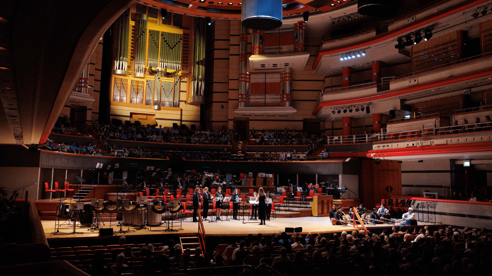 SFE Ensembles performing on stage at Symphony Hall in Birmingham, with musicians playing to a large seated audience inside the concert hall.