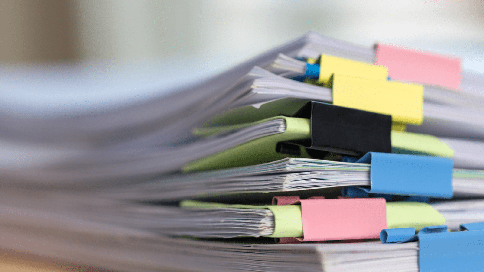 A stack of school or office documents organised with colourful binder clips.