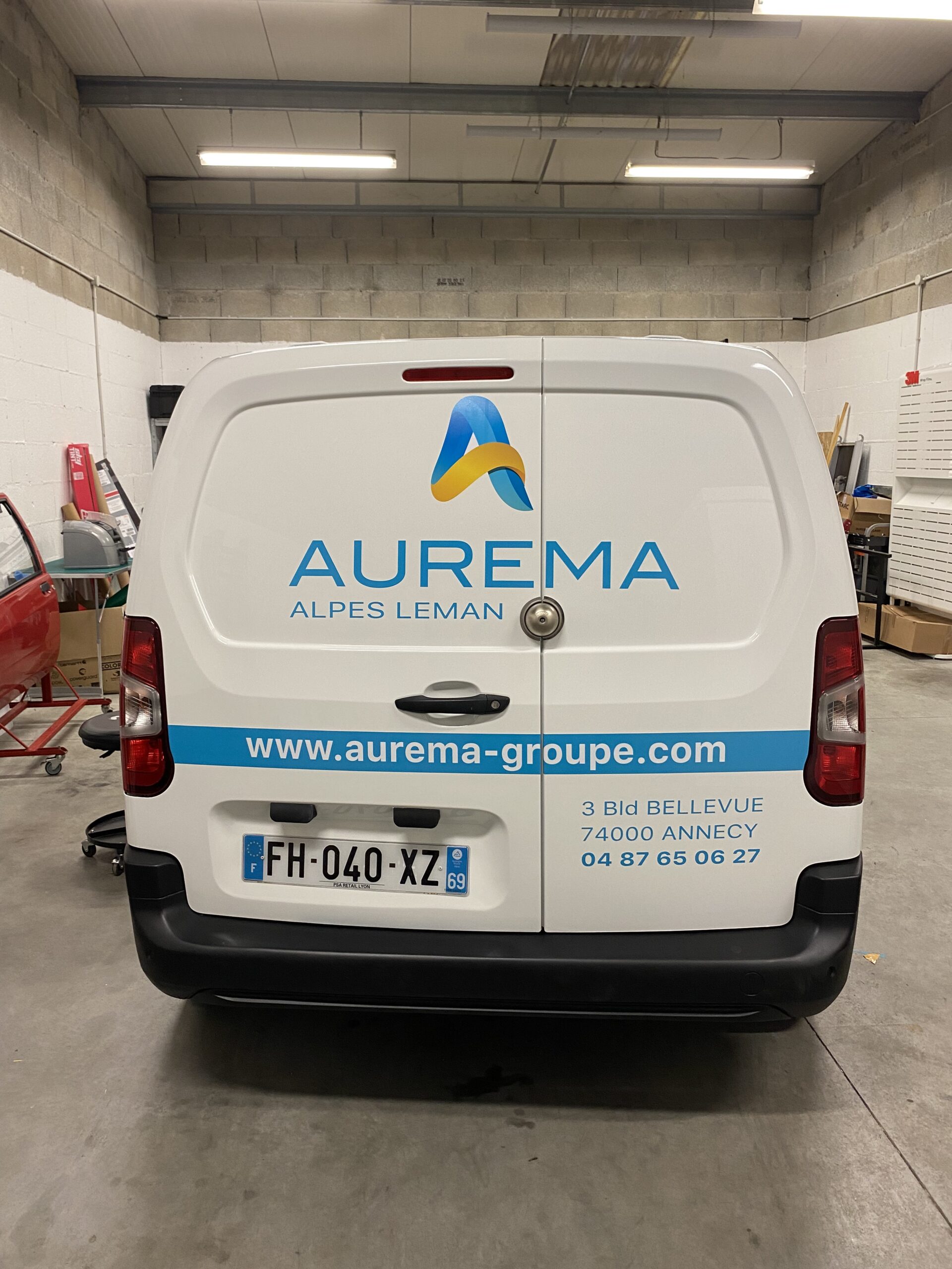 Flocage d'un peugeot partner blanc pour l'entreprise AUREMA vue du coffre marquage sur embouti logo et moyens de communications avec les couleurs de la société