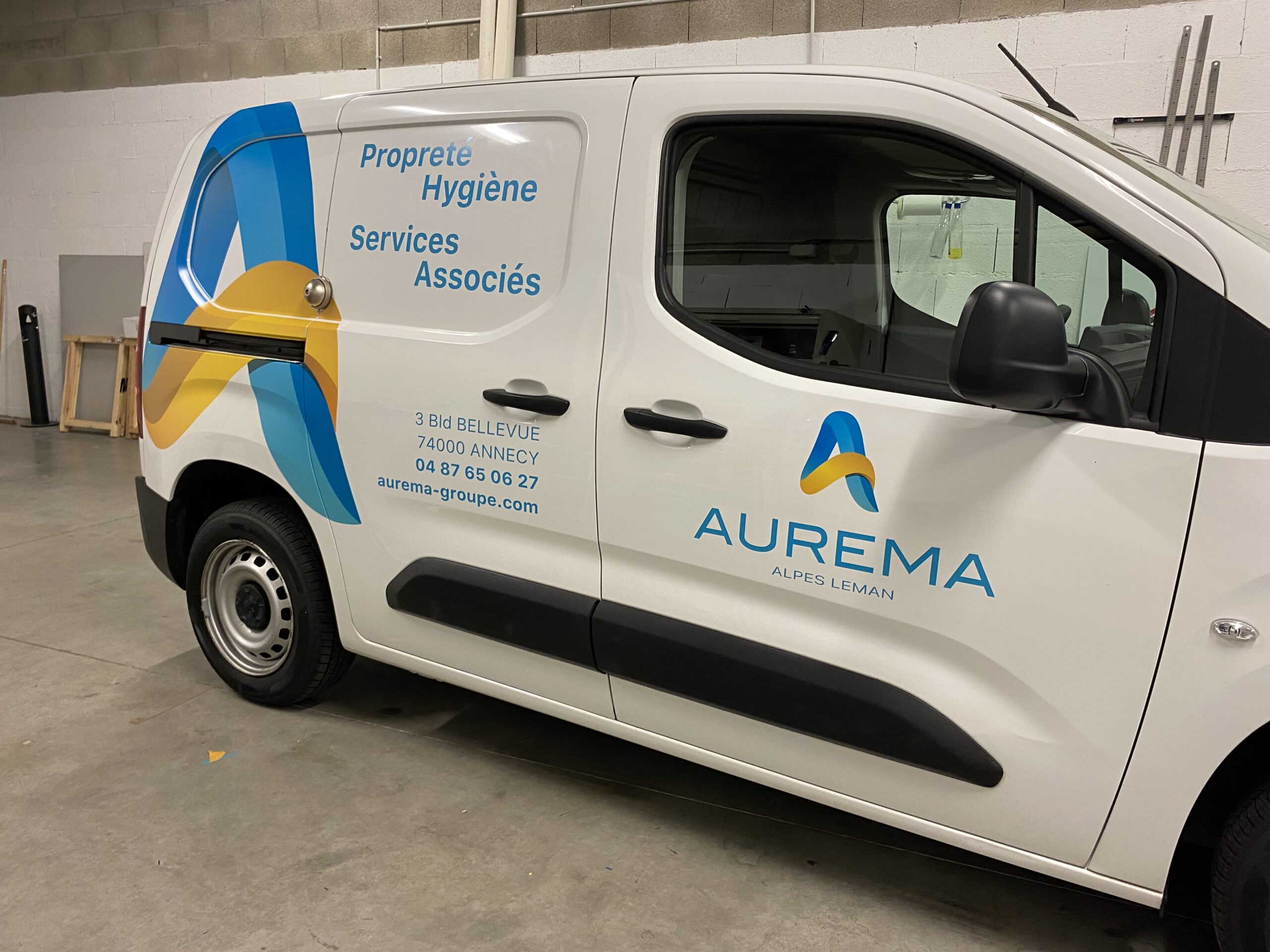 Marquage publicitaire sur un véhicule blanc pour l'entreprise AUREMA vue de profil avec logo et activité de l'entreprise couleurs jaune et bleue