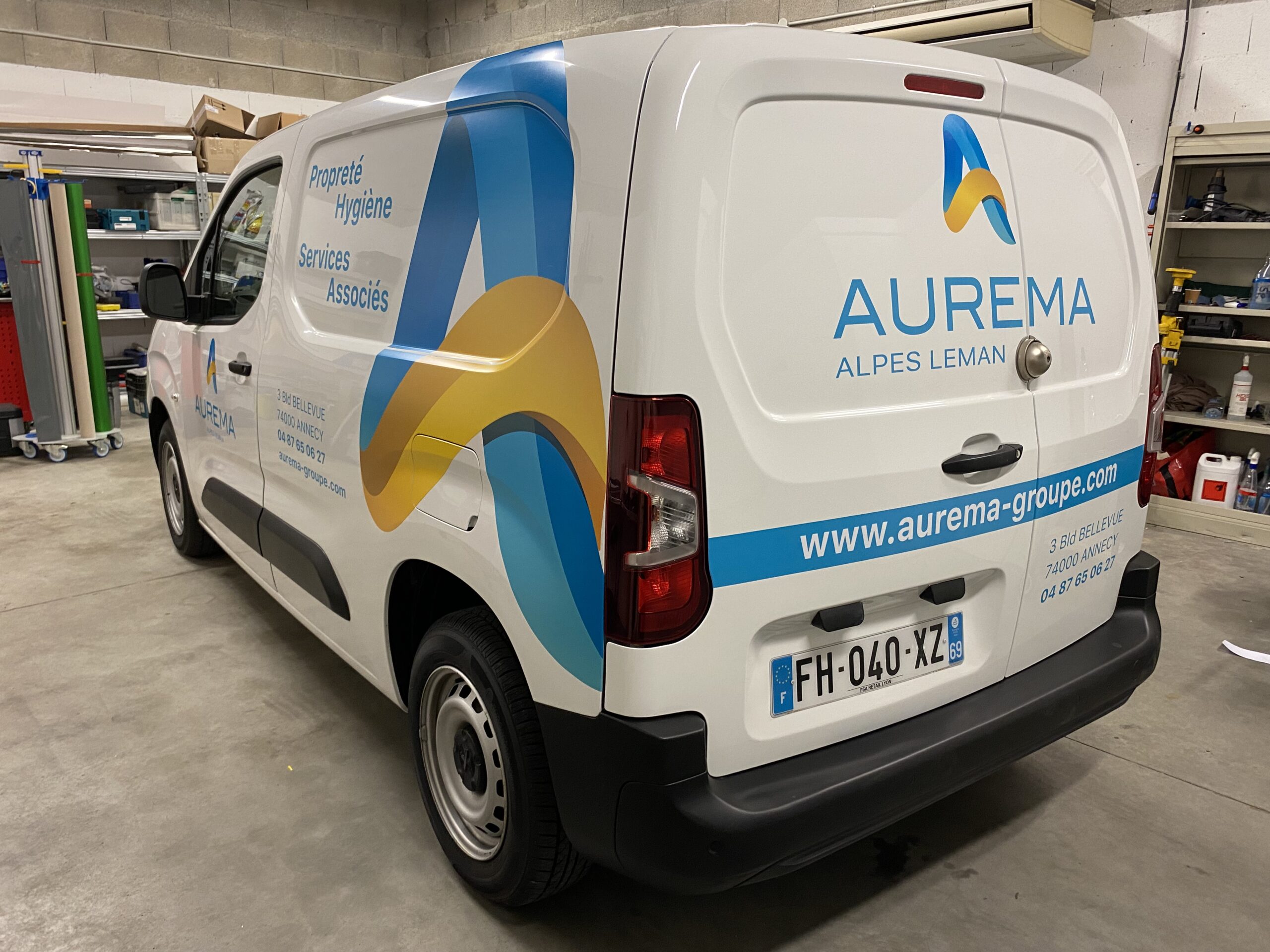 Flocage d'un peugeot partner blanc pour l'entreprise AUREMA vue arrière de 3/4 avec logo et moyens de communication, couleurs jaune et bleue