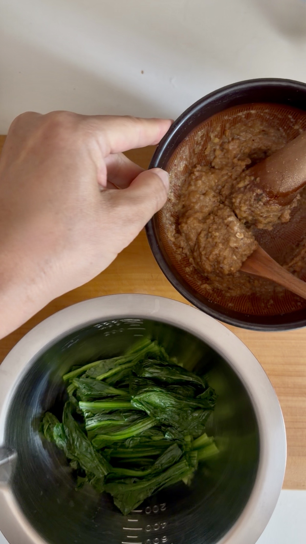 Two plates showing spinach and crushed walnuts, prepared for a Japanese-style spinach and walnut dish